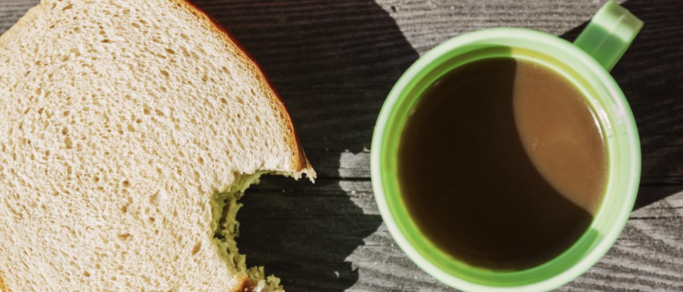 En skalad mandarin, en halväten smörgås och en kaffekopp på ett träbord.