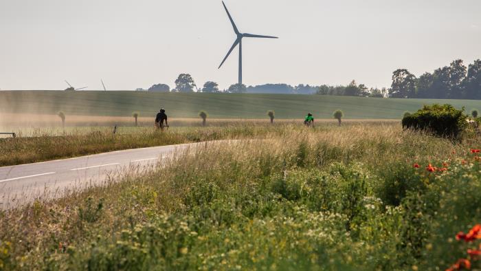 Ett åkerlandskap med en cyklist. Längre bort syns ett vindkraftverk.