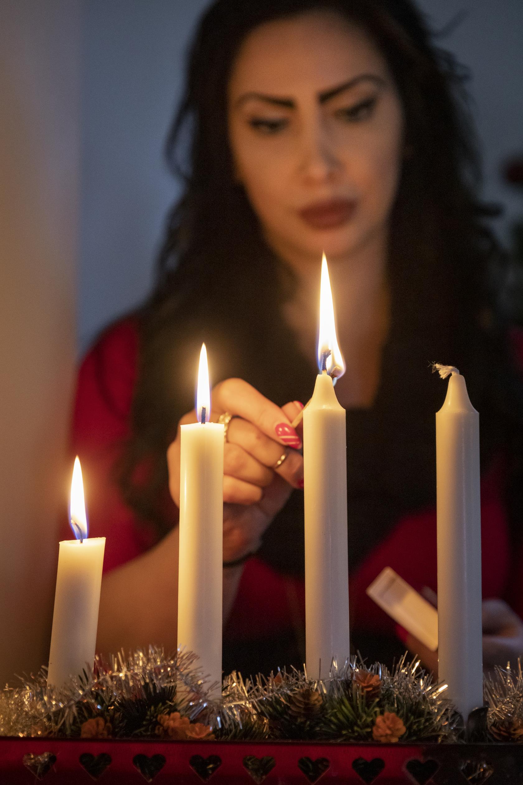 En kvinna tänder tredje ljuset i en adventsljusstake.