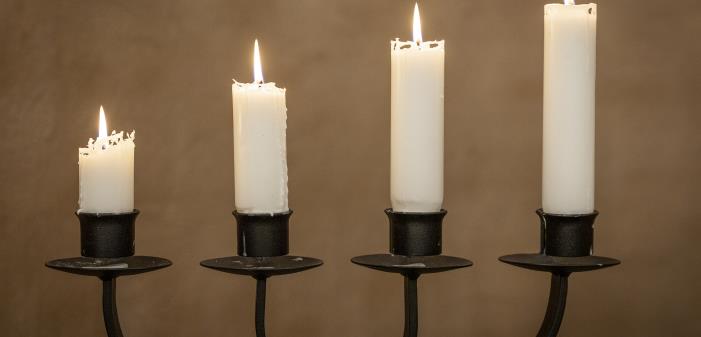 En adventsljusstake i svart smide med alla fyra ljusen tända.