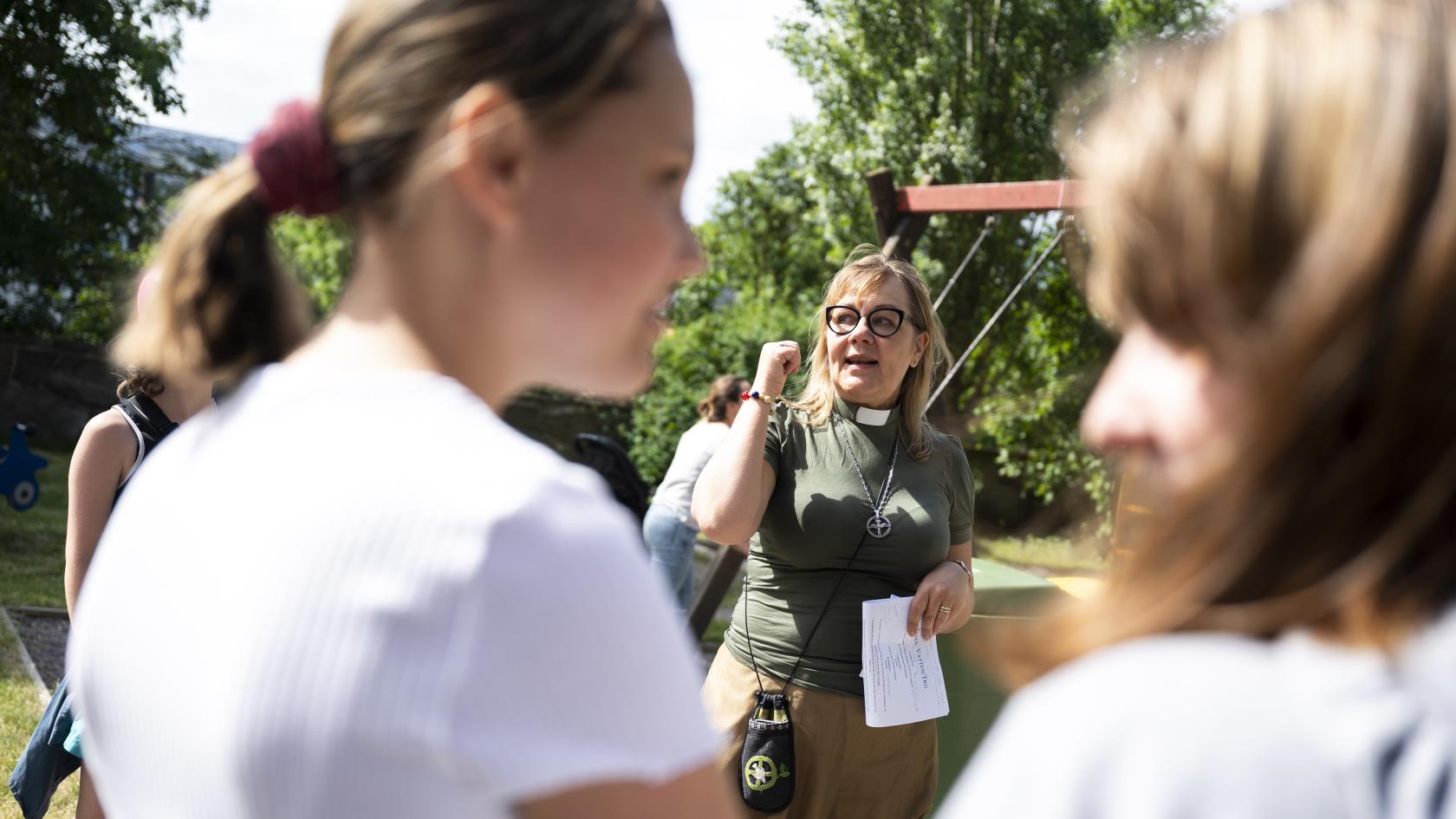 En kvinnlig diakon pratar med ungdomar utomhus en sommardag.