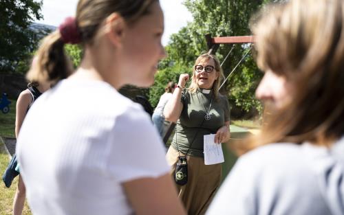 En kvinnlig diakon pratar med ungdomar utomhus en sommardag.