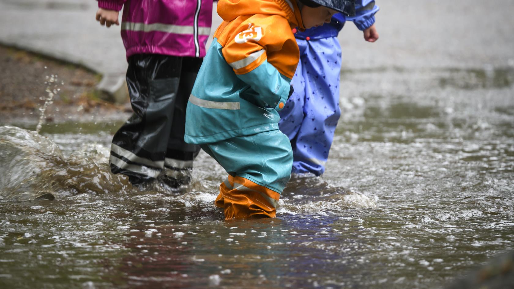 Barn i färggranna regnkläder plaskar i en vattenpöl.