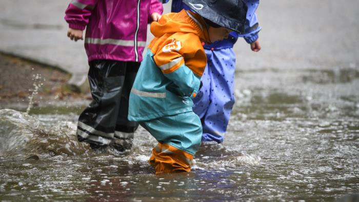 Barn i färggranna regnkläder plaskar i en vattenpöl.