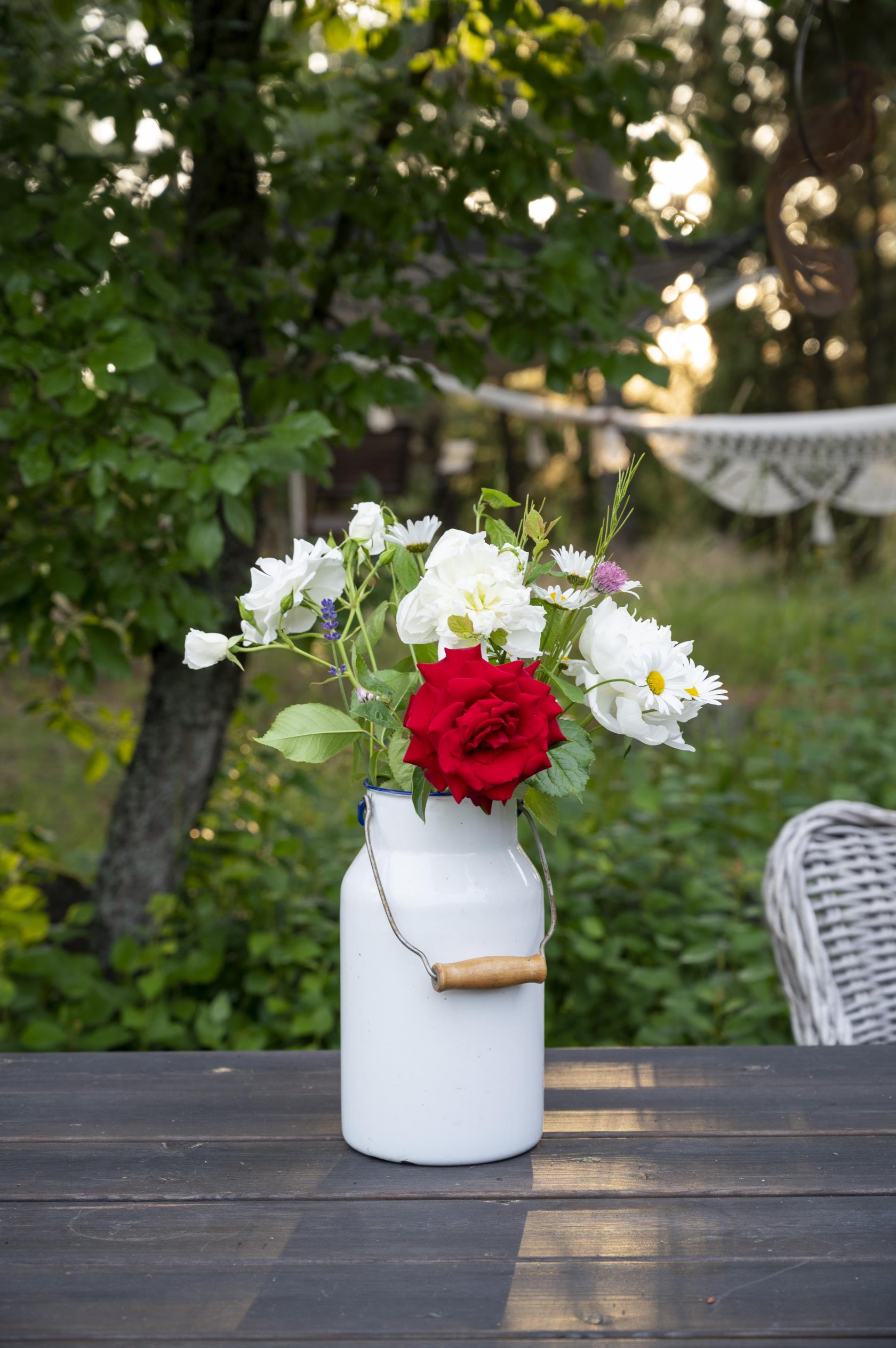 En vas med sommarblommor står på ett bord i trädgården.