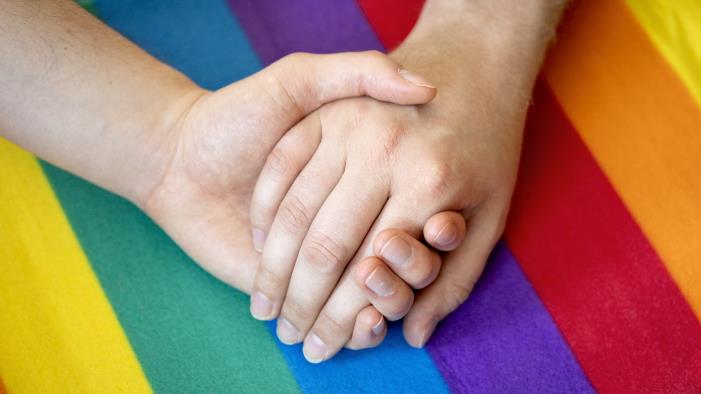 Två händer håller varandra, på ett regnbågsfärgat tyg.