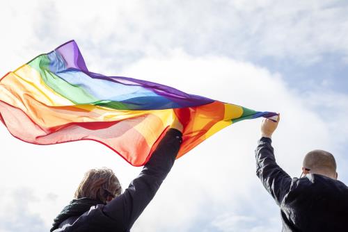 Uppsträckta händer som håller en regnbågsflagga. Illustrationsbild HBTQ-tema.