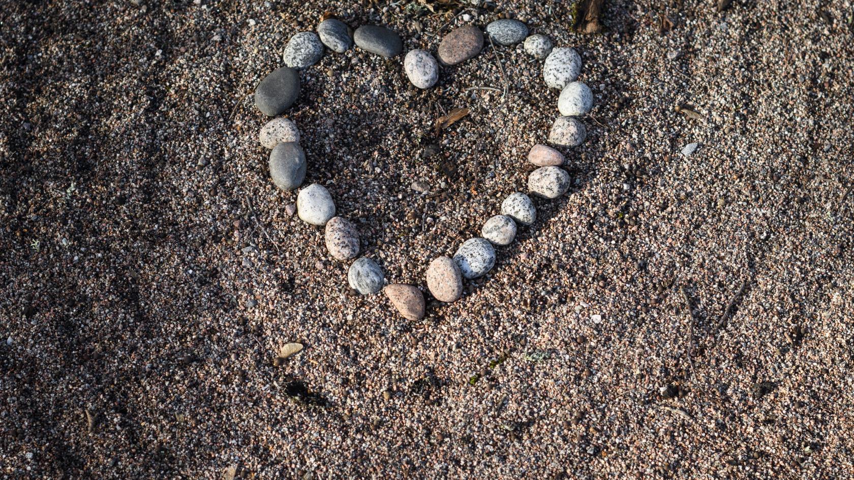 Stenar upplagda i form av ett hjärta framför en krans på en grav.