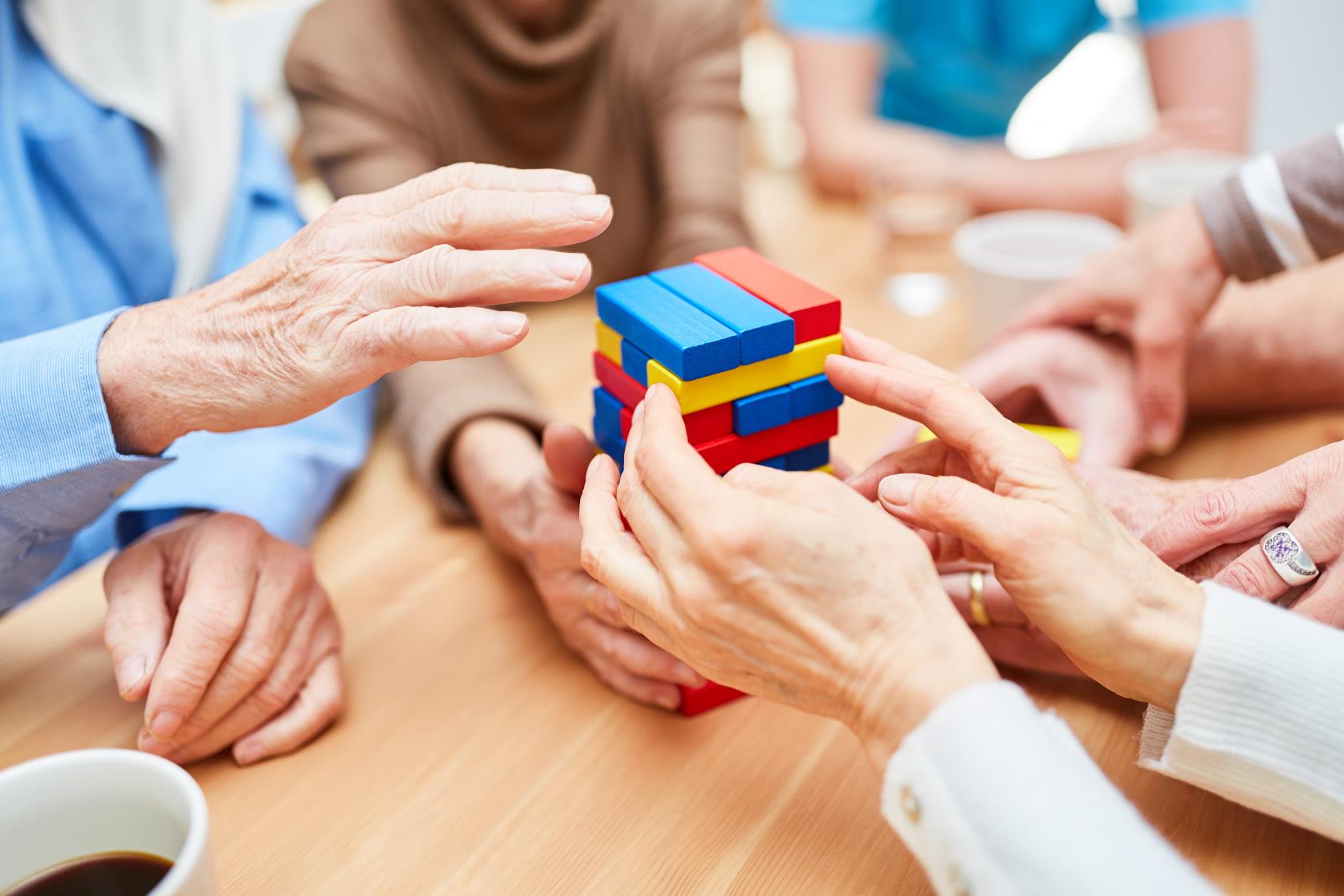 Några äldre sitter runt ett bord och spelar ett sällskapsspel med olikfärgade byggklossar som inte ska rasa.