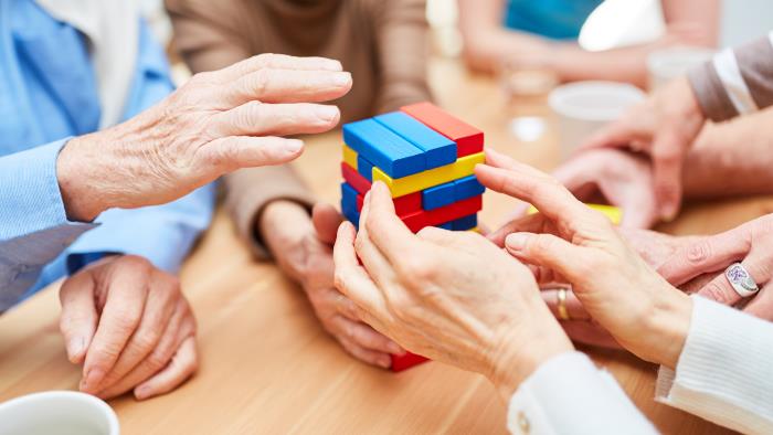 Några äldre sitter runt ett bord och spelar ett sällskapsspel med olikfärgade byggklossar som inte ska rasa.