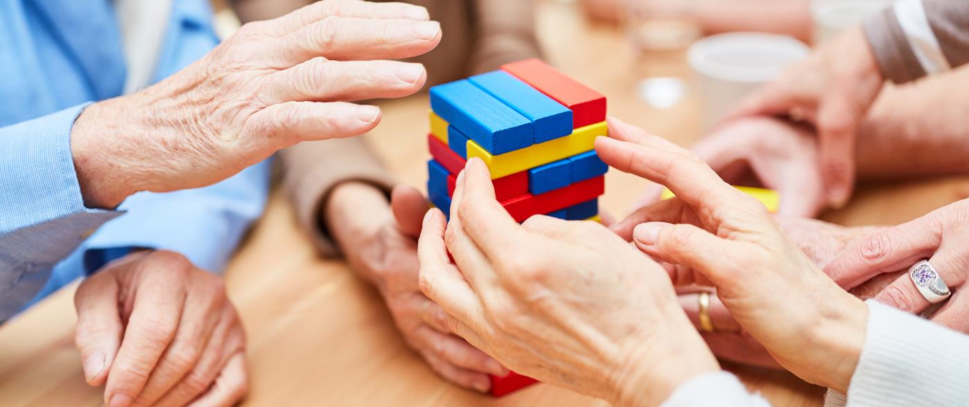 Några äldre sitter runt ett bord och spelar ett sällskapsspel med olikfärgade byggklossar som inte ska rasa.