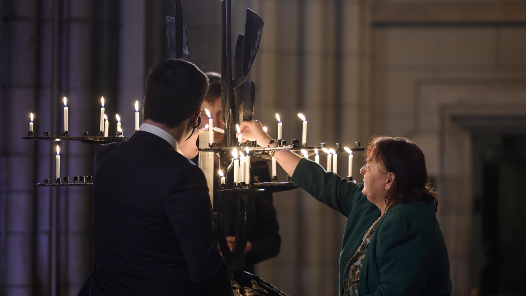 Några personer tänder ljus i järnskulpturen Folkförsoningens träd i Uppsala domkyrka.