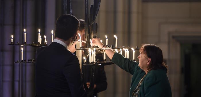 Några personer tänder ljus i järnskulpturen Folkförsoningens träd i Uppsala domkyrka.