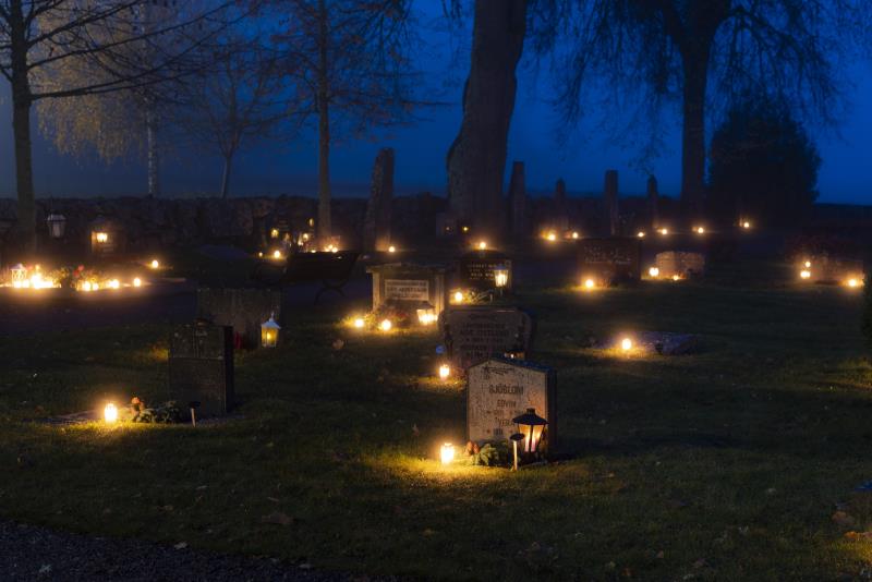 Ljuslyktor lyser på en kyrkogård.