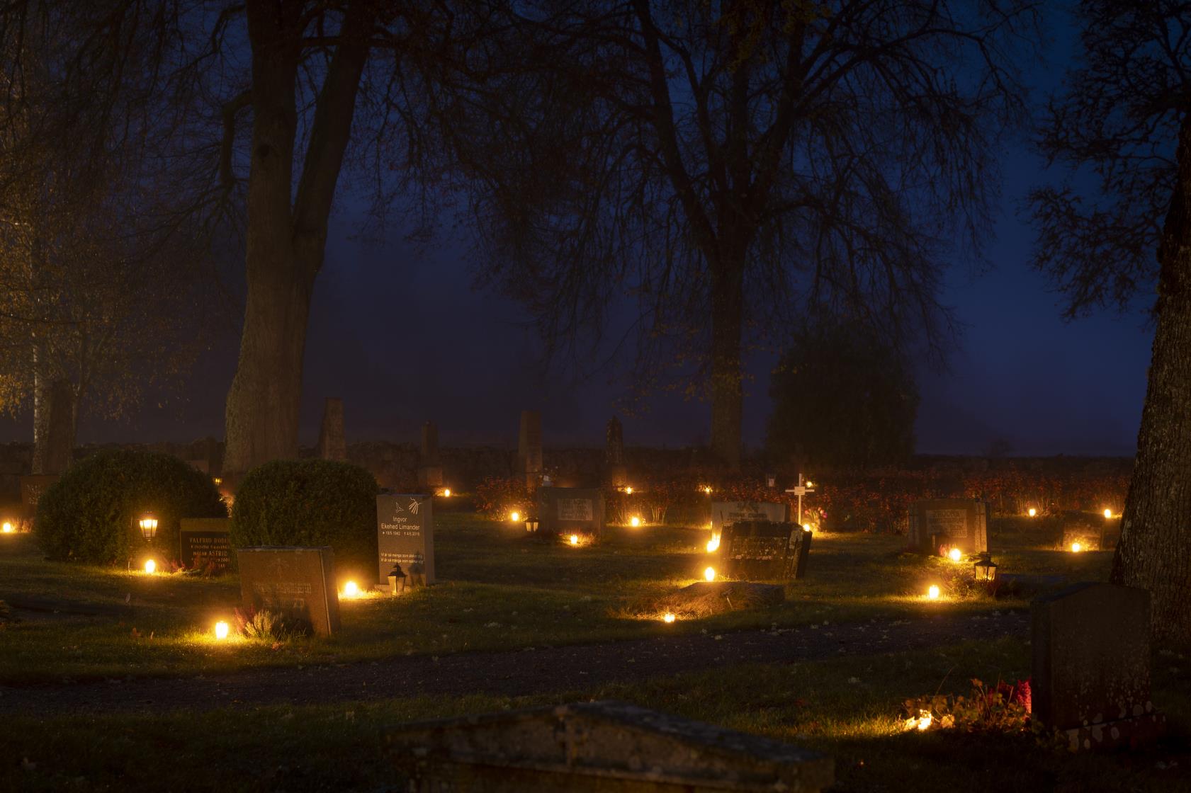 Ljuslyktor lyser på en kyrkogård.