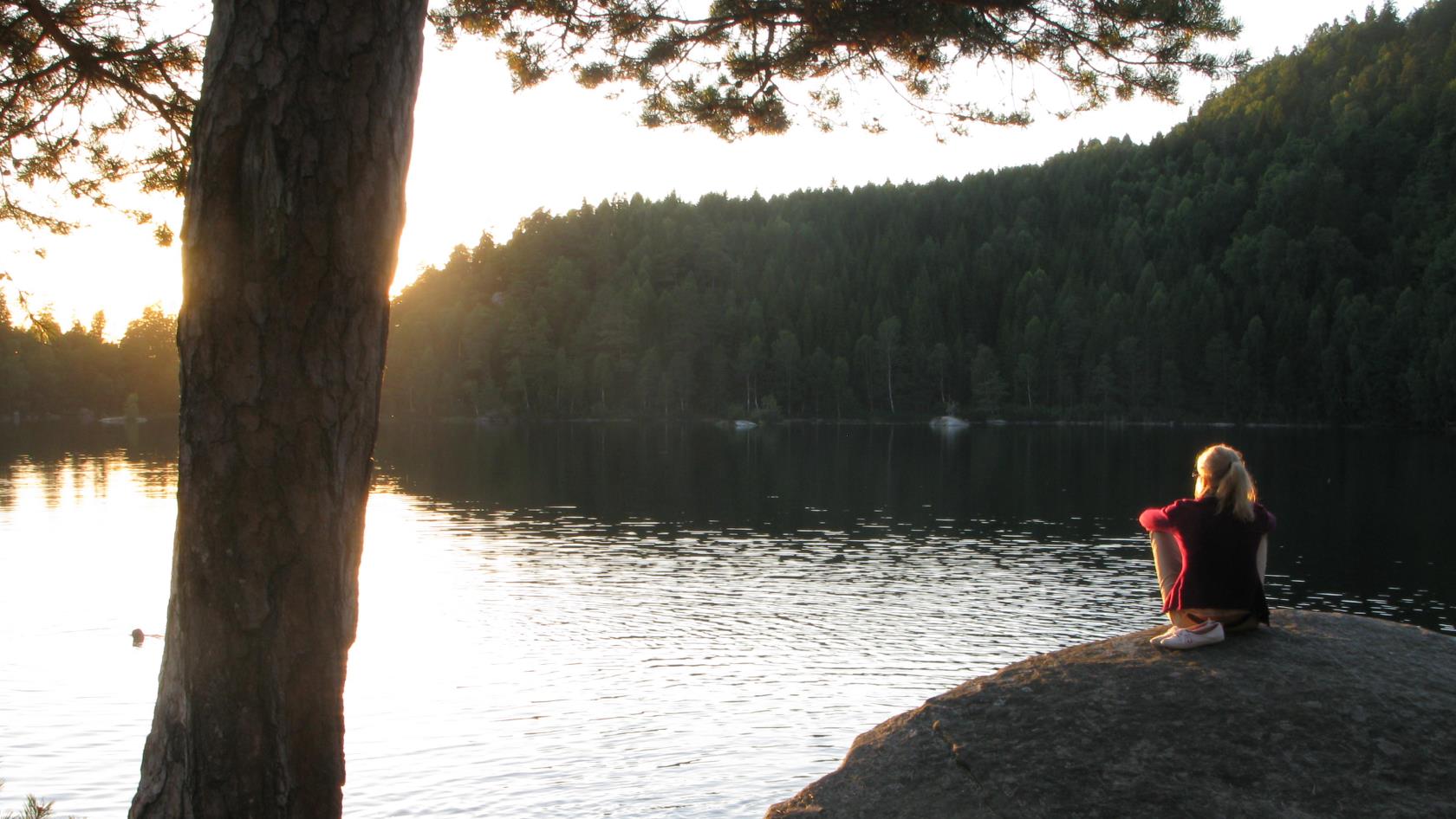 En kvinna sitter på en klippa och tittar på solnedgången.