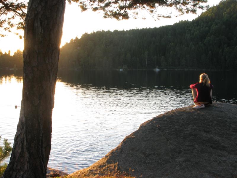 En kvinna sitter på en klippa och tittar på solnedgången.