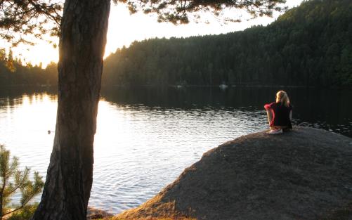 En kvinna sitter på en klippa och tittar på solnedgången.