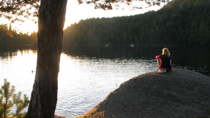 En kvinna sitter på en klippa och tittar på solnedgången.