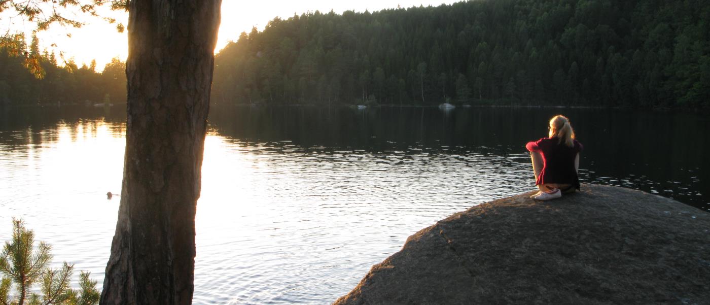 En kvinna sitter på en klippa och tittar på solnedgången.