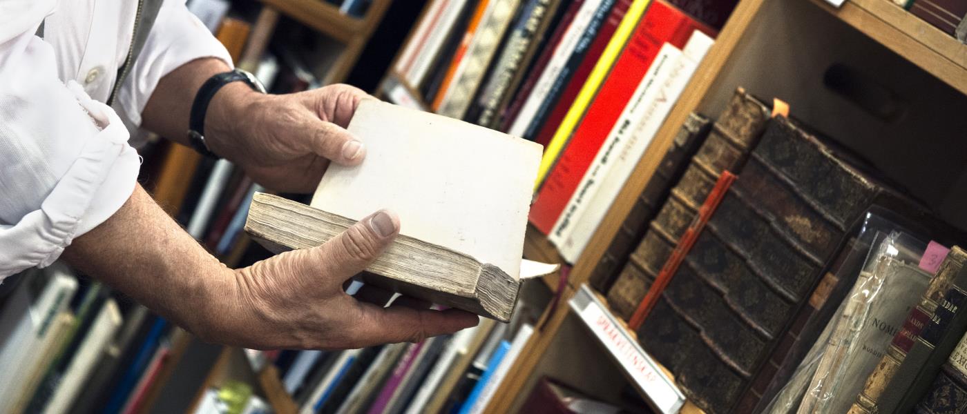 Någon bläddrar i en gammal bok från en bokhylla i ett bibliotek.