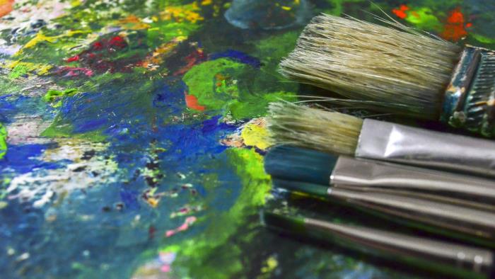 Närbild av målarpenslar på en palett fylld av torkad färg.