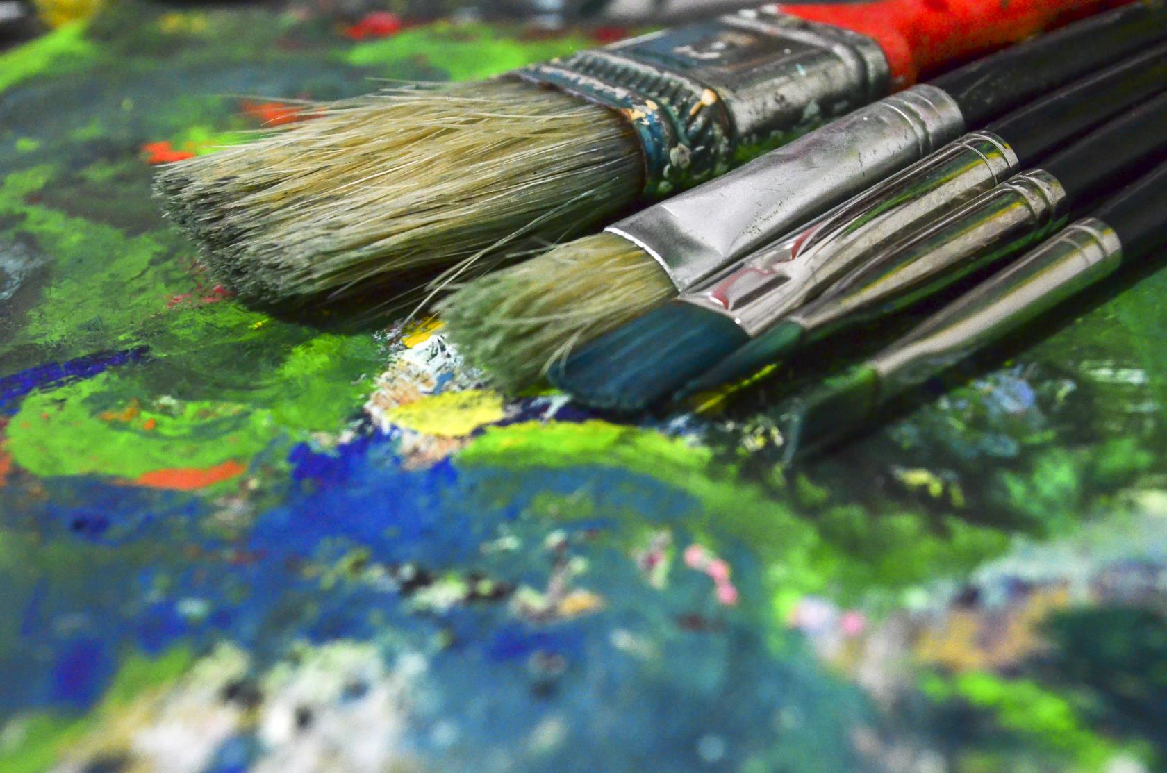 Närbild på målarpenslar på en palett fylld av torkad färg.