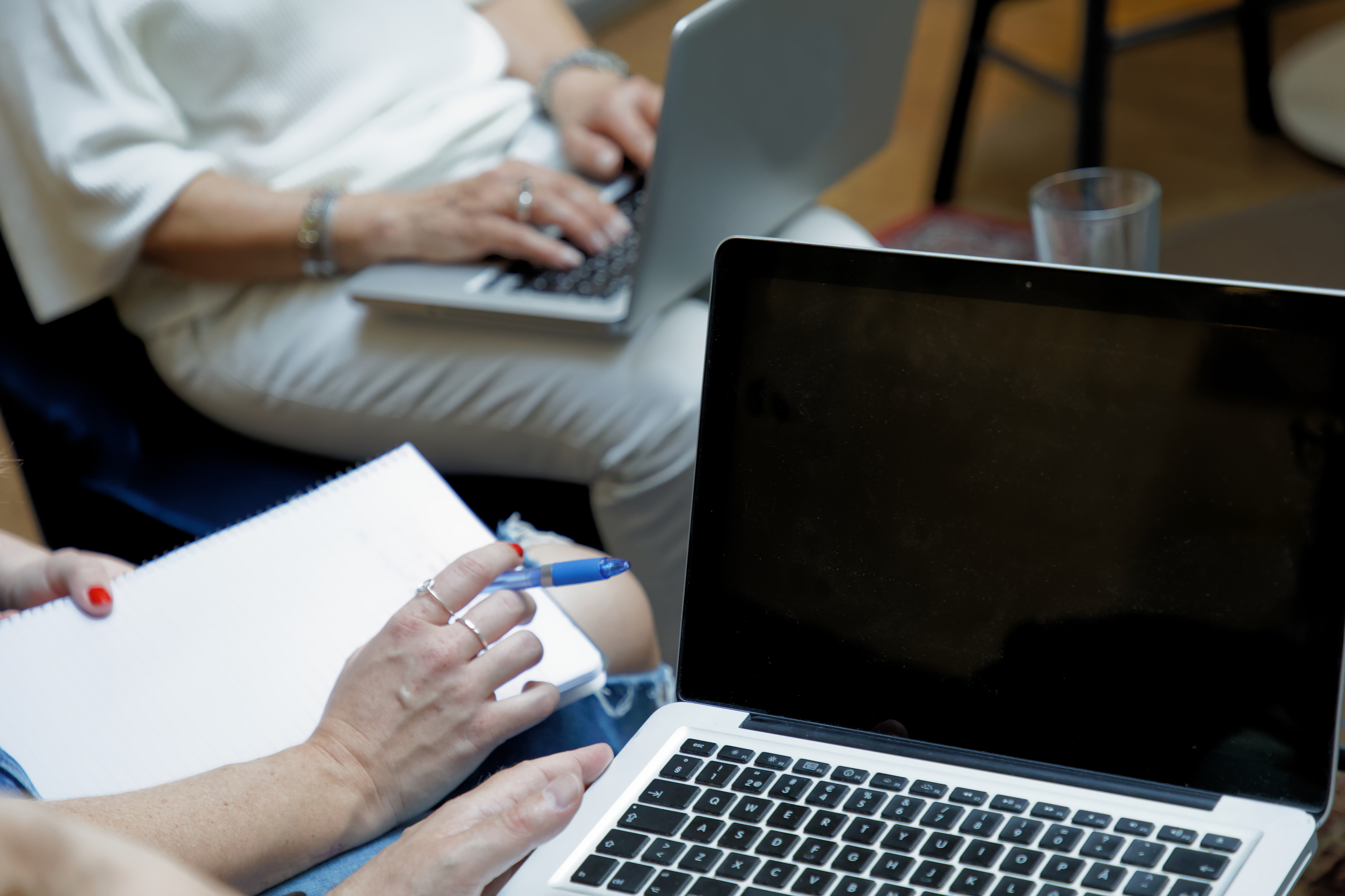 Några personer sitter med laptops och anteckningsblock i knät.