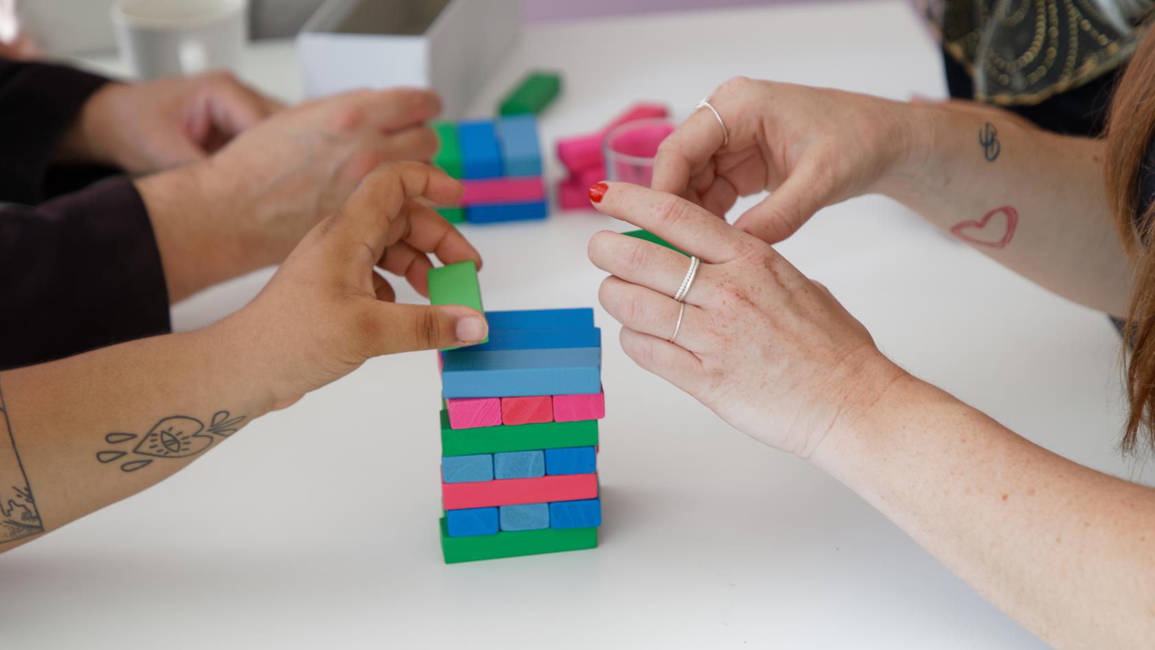 Några personer spelar Jenga med färggranna klossar.