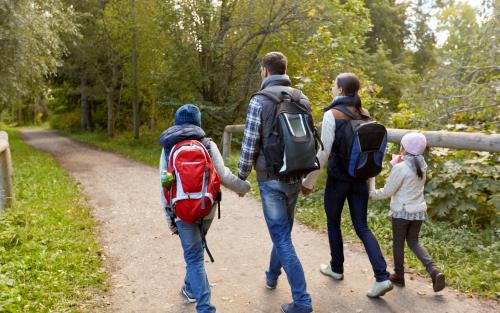 En familj med två barn går hand i hand på en vandringsled i skogen.