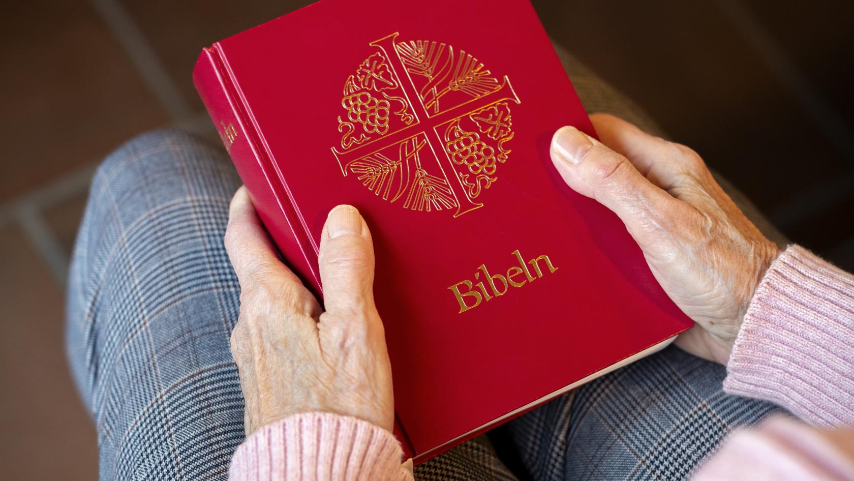 En person sitter i en kyrkbänk med en bibel i knät.