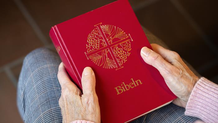 En person sitter i en kyrkbänk med en bibel i knät.