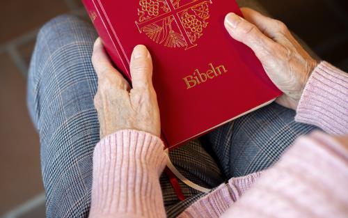 En person sitter i en kyrkbänk med en bibel i knät.