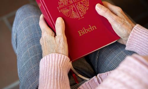 En person sitter i en kyrkbänk med en bibel i knät.