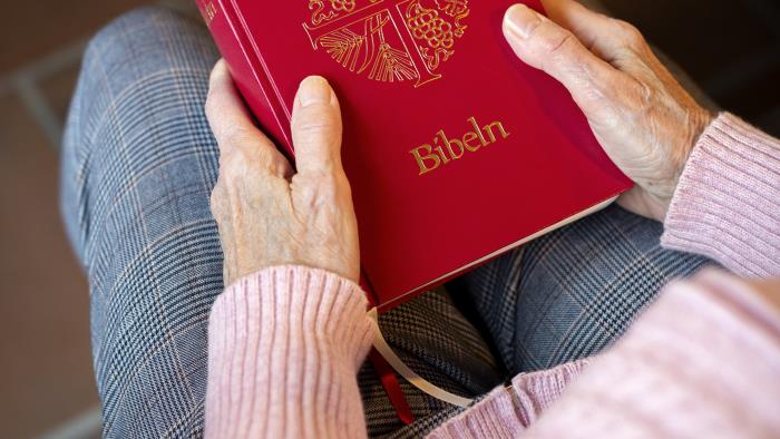 En person sitter i en kyrkbänk med en bibel i knät.