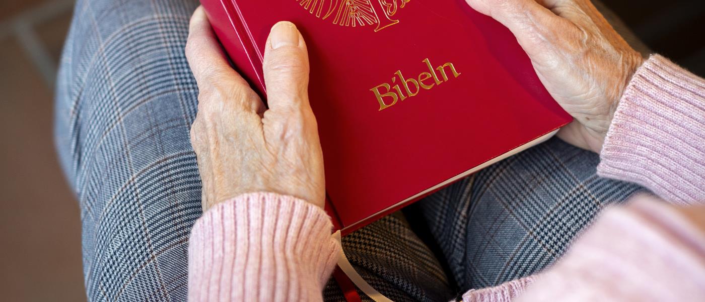 En person sitter i en kyrkbänk med en bibel i knät.