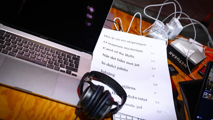 På ett skrivbord står en dator med hörlurar och en lista med julsånger på ett papper.