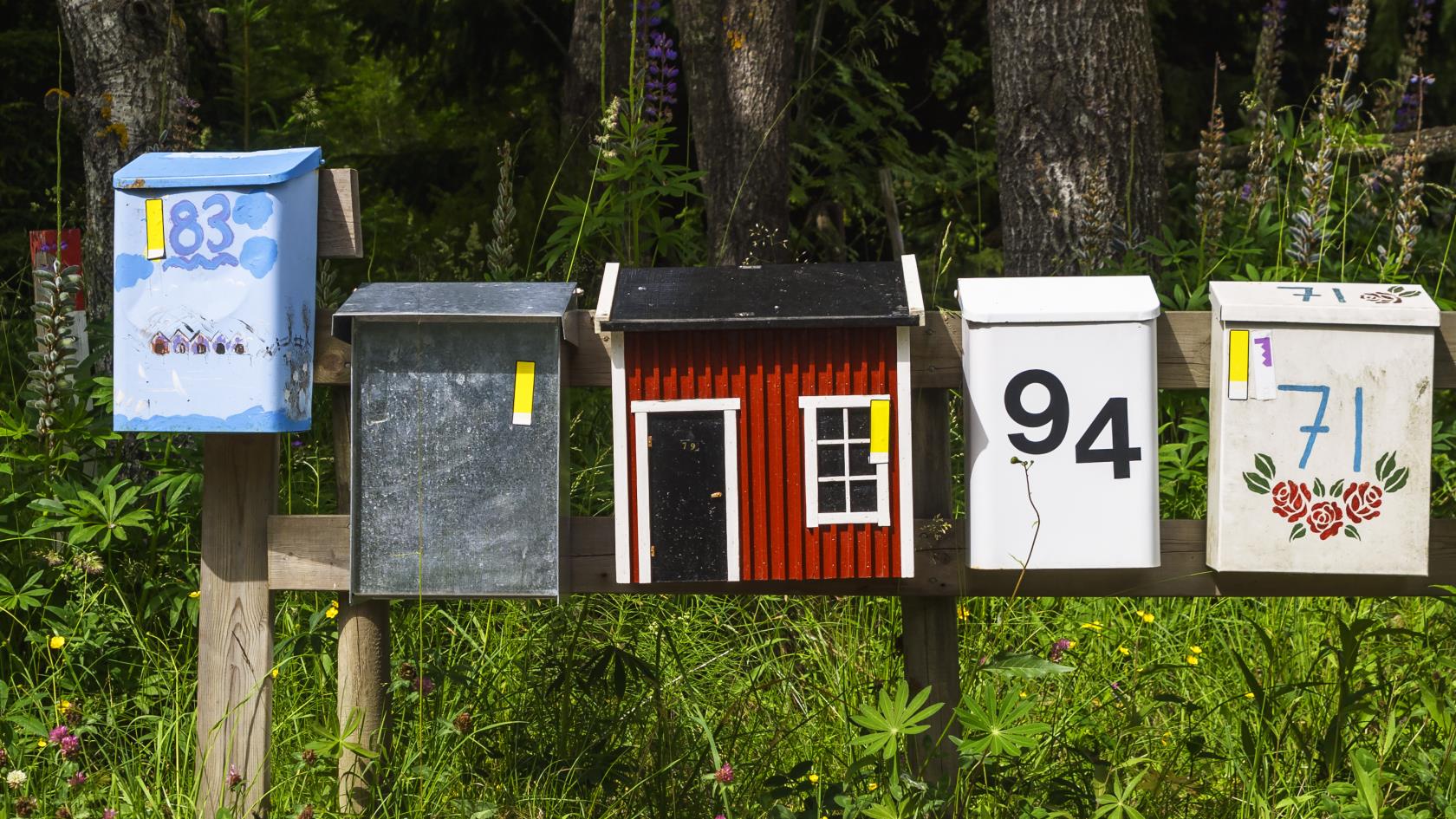 Fem färgglada brevlådor bredvid varandra. Kanske till sommarstugor.