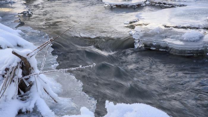 Vatten strömmar genom en delvis isbelagd fors.