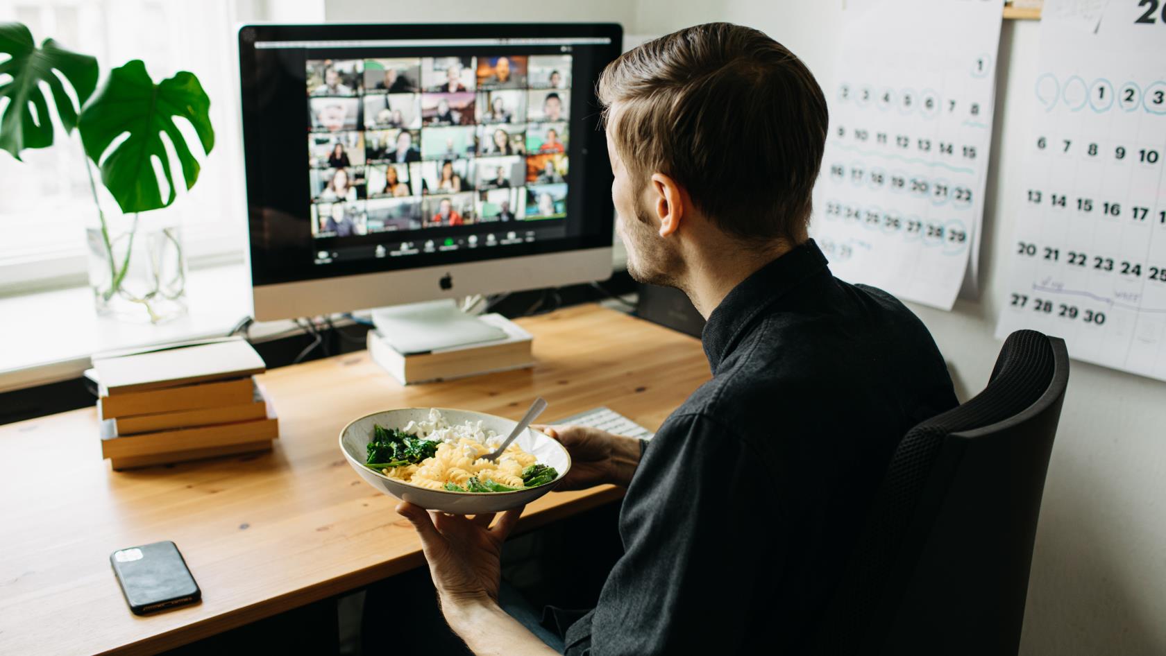 En man äter lunch vid datorn medan han deltar i ett video-möte.