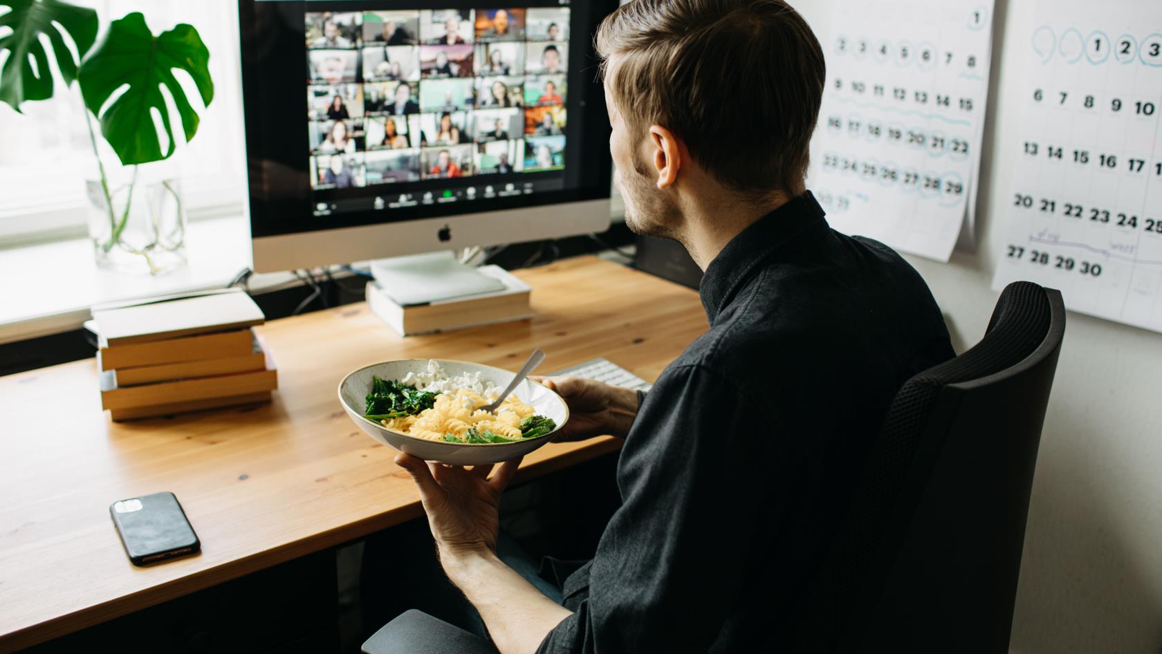 En man äter lunch vid datorn medan han deltar i ett video-möte.