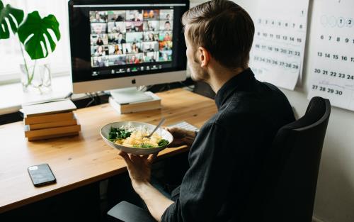 En man äter lunch vid datorn medan han deltar i ett video-möte.
