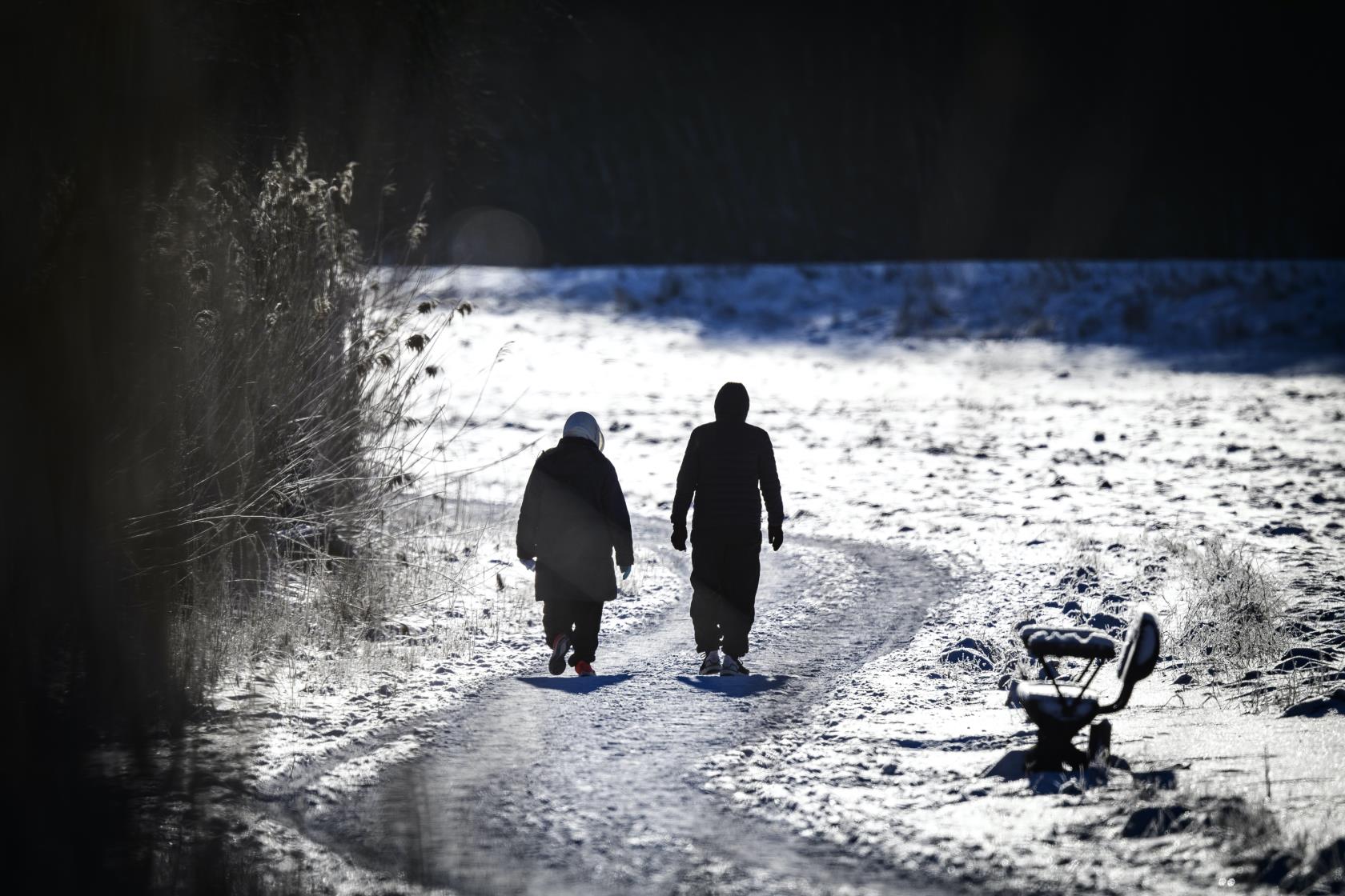 Två personer är ute på långpromenad. Det är vinter och solen skiner.