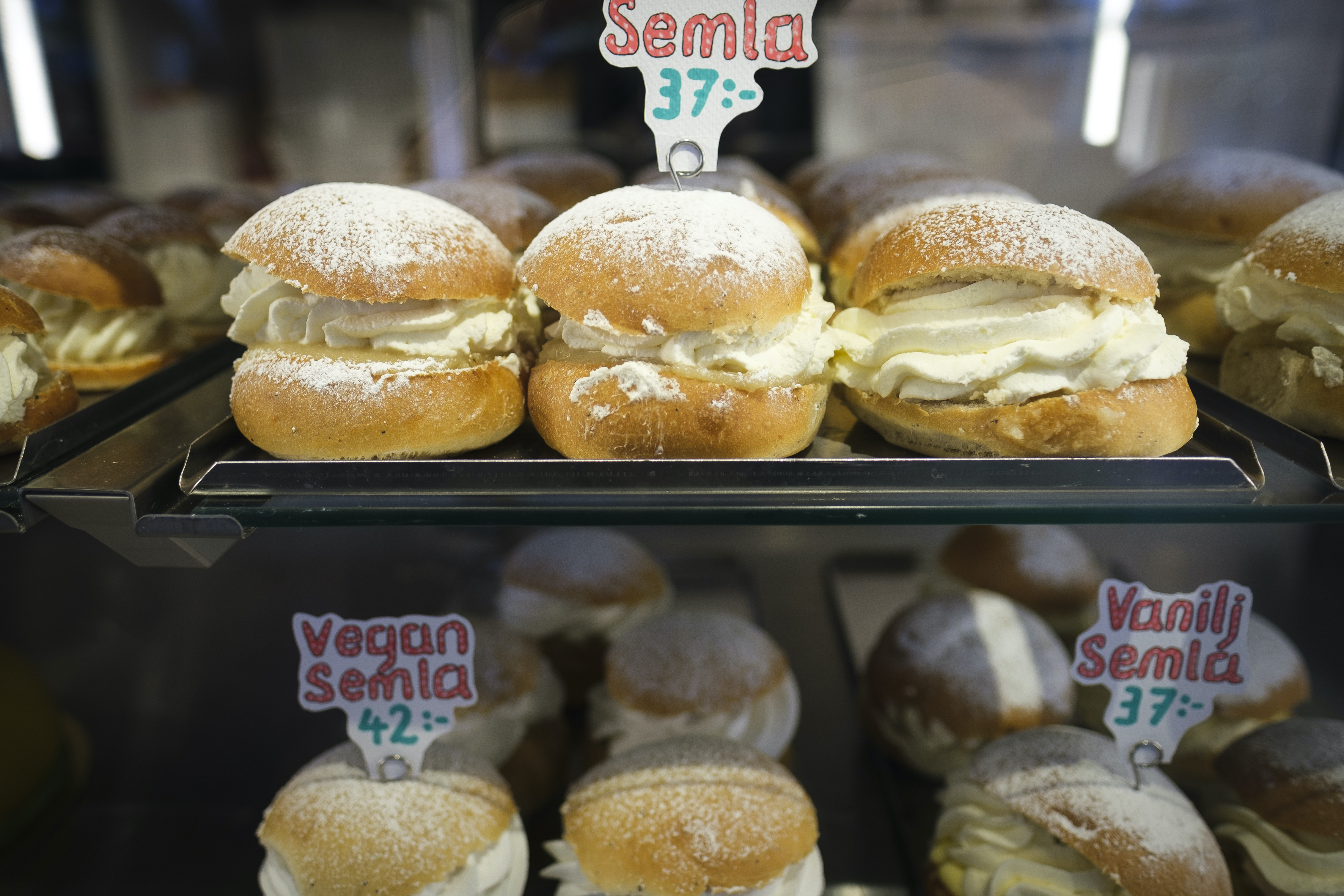 Olika sorters semlor står uppställda på ett konditori.