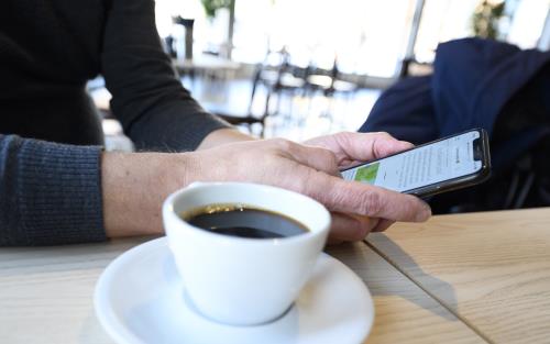 En person sitter med sin mobiltelefon och dricker kaffe.