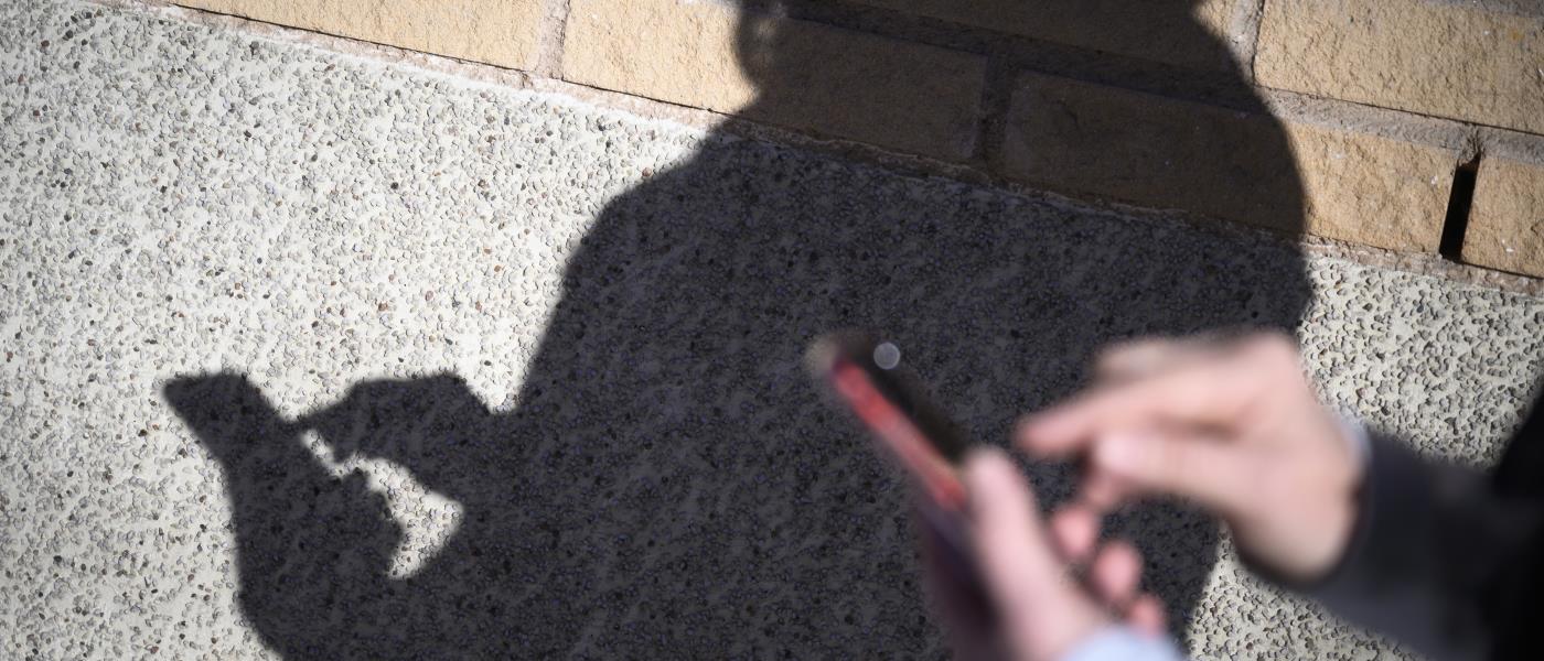En skugga på en tegelvägg av någon som skriver på sin mobiltelefon.