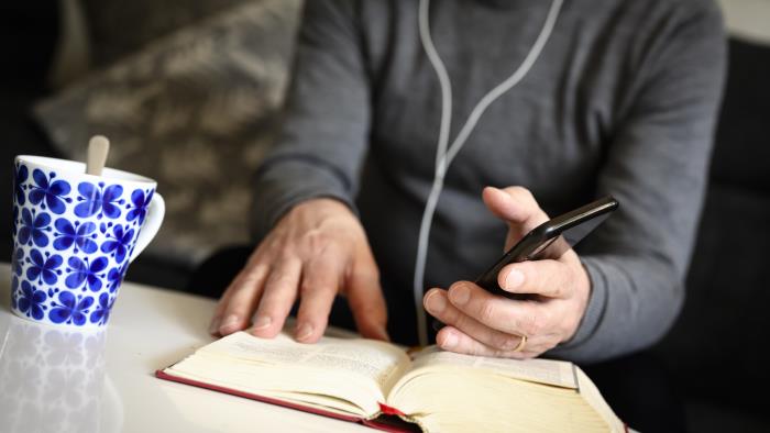 En präst sitter med hörlurar och pratar i mobiltelefon med bibeln uppslagen framför sig.