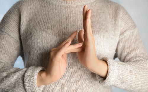 En kvinna i stickad tröja talar teckenspråk mot kameran.