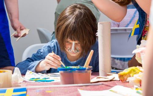 Ett barn med ansiktet målat som en katt sitter och målar vid ett bord.