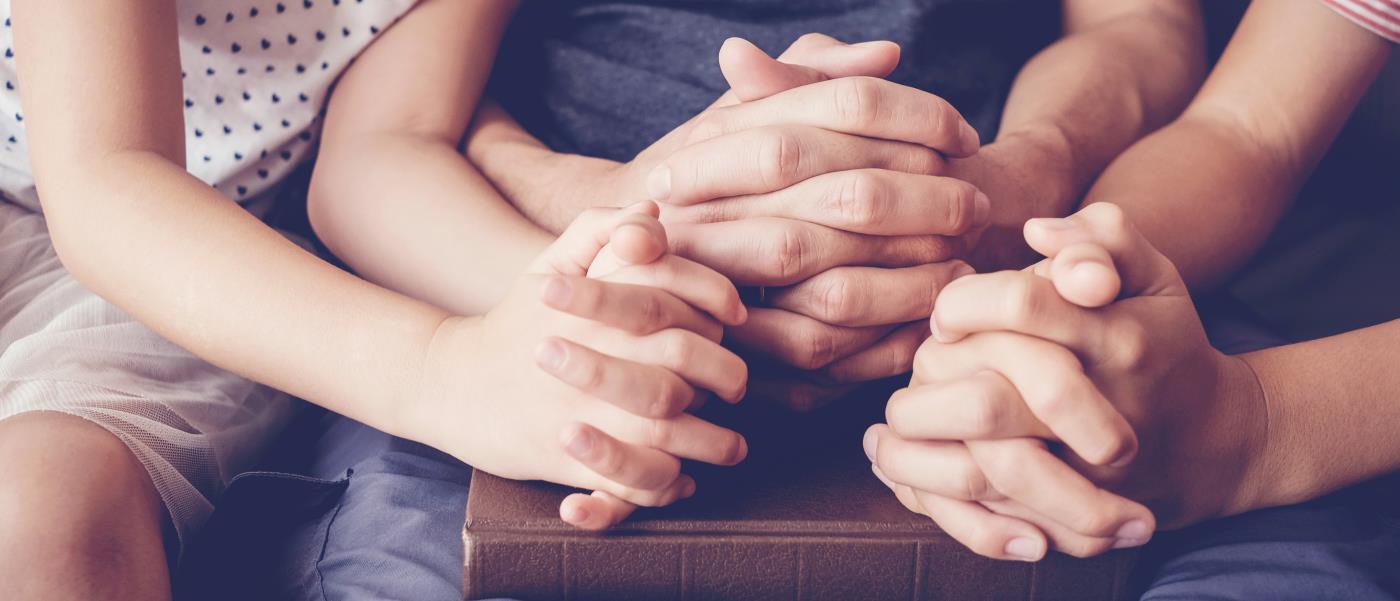 En vuxen och två barn sitter med händerna knutna i bön.